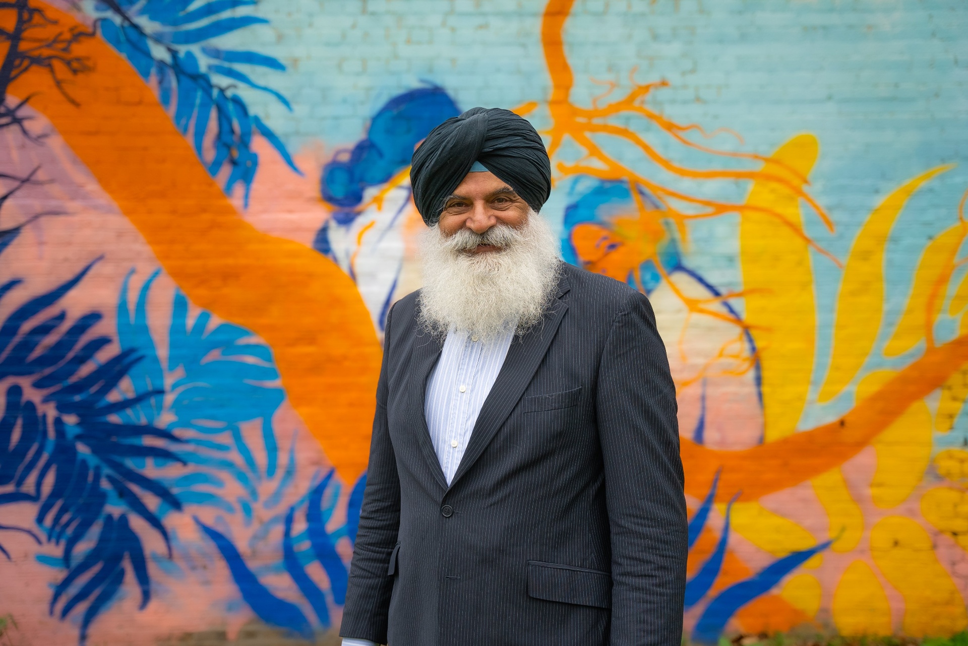 Older man smiling in front of a colourful mural